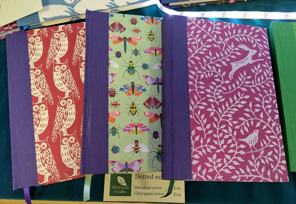 Left to right: owl against a red background, with purple bookcloth; insects against a green background with purple bookcloth; hare and wren against a magenta background, purple bookcloth.